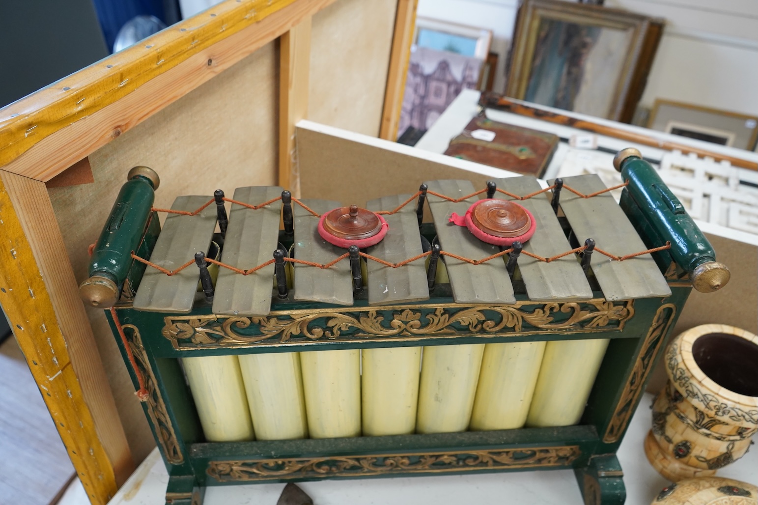 A green and gold painted wooden Javanese Gamelan Slenthem musical instrument, 61cm wide, 46cm high, together with two hammers